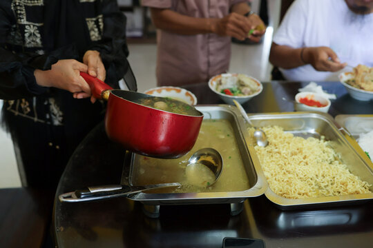 People preparing and serving traditional indonesian bakso meatball soup from large metal trays for a gathering