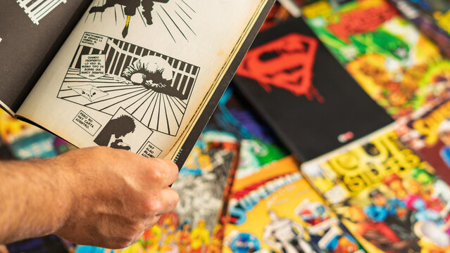 Guayaquil, Ecuador &ndash; August 10, 2024: Person reading a vintage comic book over a collection of superhero comics, reflecting nostalgia, reading habits and pop culture fandom.