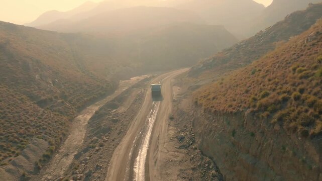 Aerial shot of a dump truck traveling a muddy haul road through a remote, rugged desert mining canyon.