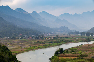 Naklejka premium A scenic view of Song Mien River flowing through a valley in Quan Ba, Ha Giang, Vietnam, with mountains in the background and a small boat carrying people on the water near Cao Bang in Vietnam.