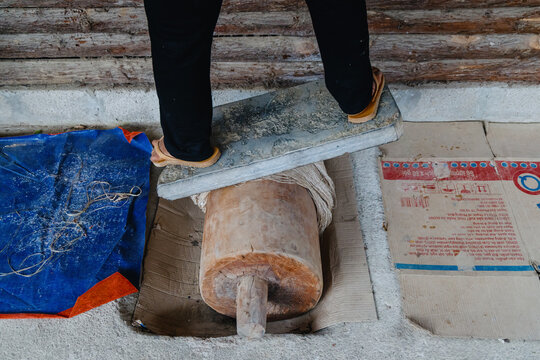 In Quan Ba, Ha Giang, Vietnam a person in black pants and sandals uses a stone to press a reed. This is likely part of a traditional process or craft in the area. ,