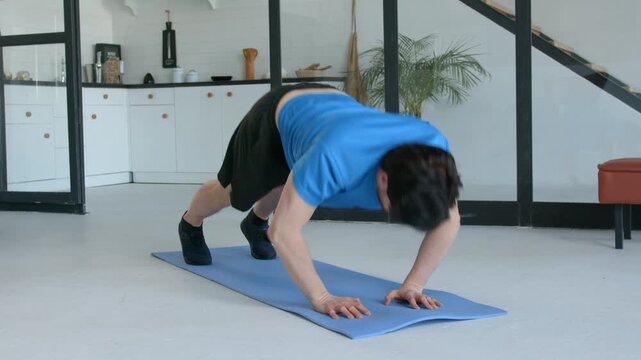 Determined sporty fit man performing pike push up exercise, strengthening shoulder muscles and improving core stability while working out in domestic room.