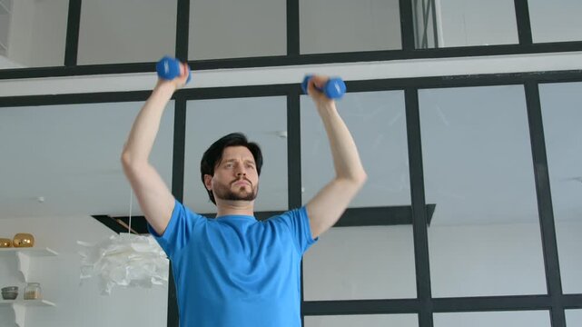 Determined handsome sporty fit man practicing dumbbell standing shoulder press, improving strength in chest, shoulders, deltoids, and triceps during indoor sports training