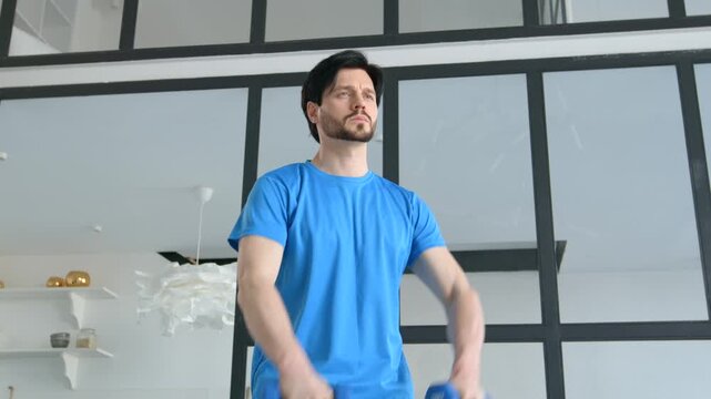 Active sporty muscular build man practicing dumbbell front raise to lateral raise exercise, strengthening middle deltoids and anterior deltoids of shoulders indoors.