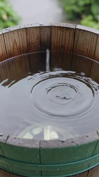 Wooden rain barrel collecting rainwater with ripples, vertical footage