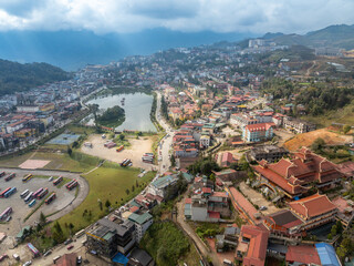 Naklejka premium Aerial view of Sapa, Vietnam, showcasing the town's architecture, lake, and surrounding mountains. Tourists visit to experience the culture and scenery.