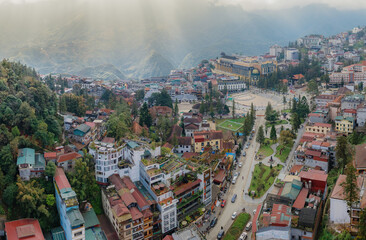 Obraz premium A panoramic view captures the bustling town of Sa Pa, Vietnam, nestled amidst rolling hills and shrouded in mist, showcasing its unique architecture.