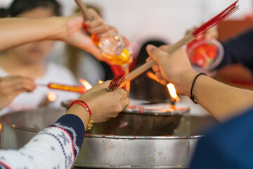 Obraz premium Multiple hands hold incense bundles and candles over a metal oil lamp, sharing a moment of collective prayer and offering.