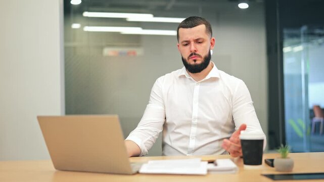 Sad bearded executive in white shirt reading letter from envelope. Businessman showing disappointment and frustration after receiving bad news or rejection at office desk.