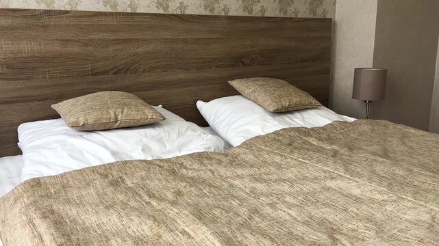 Bedroom interior. Bed covered with brown bedspread, white pillows. On the sides of the wide bed there are bedside tables with table lamps. Quiet calm atmosphere.