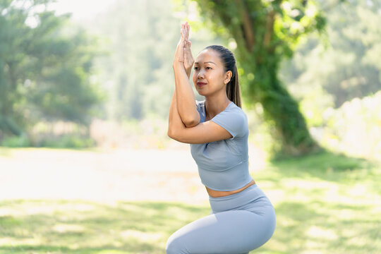 Asian woman yoga meditation outdoor park fitness balance stretching concentration focus in eagle pose during morning practice, calm expression, healthy lifestyle in green nature