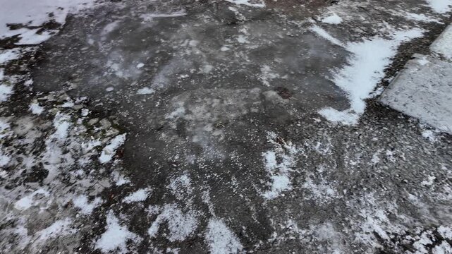 Early spring thaw on a frozen road. Footprints and tracks mark the slippery, melting ice.