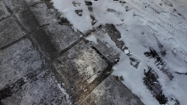 Early spring thaw on a frozen road. Footprints and tracks mark the slippery, melting ice.