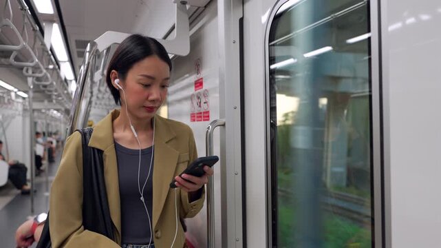 Asian woman using smartphone during morning commute on a city train, Young asian professional starting her day on the skytrain.