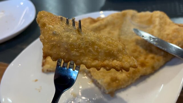 A person's hand a piece of pasty with a fork and lifts it up to eat. Fried pasties with meat filling on a white plate. Hearty lunch.
