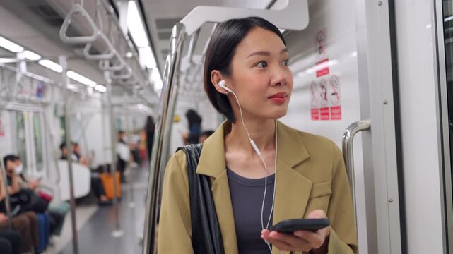 Asian woman using smartphone during morning commute on a city train, Young asian professional starting her day on the skytrain.