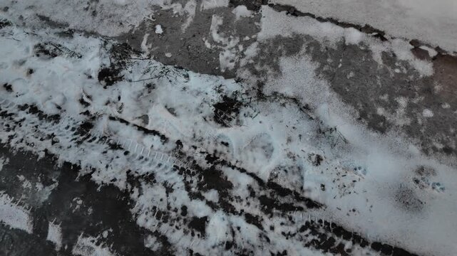Early spring thaw on a frozen road. Footprints and tracks mark the slippery, melting ice.