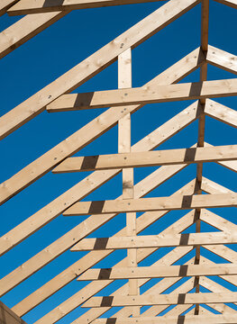 Wooden roof truss construction frame against a clear blue sky