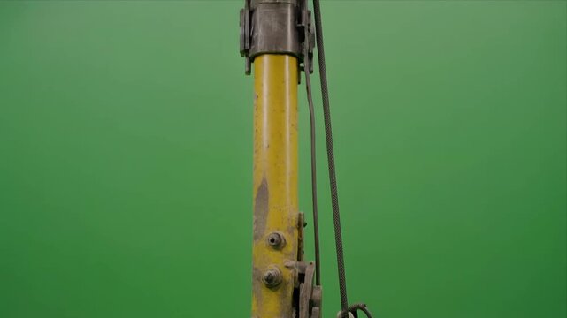 Old yellow hydraulic drilling rig closeup against green screen.