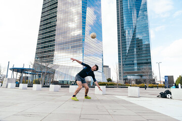 Young man doing freestyle soccer tricks with a ball outdoors, with modern skyscrapers forming the background in madrid © Koldo_Studio