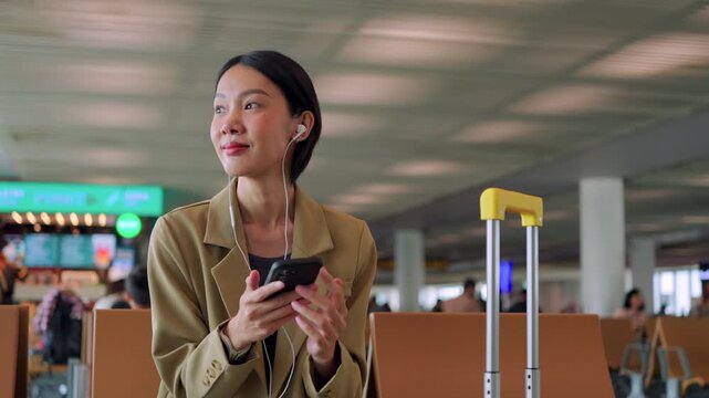 Asian woman starts her morning routine at the airport gate, listening to a podcast on her phone while waiting for departure. Concept of journey and solo travel. 