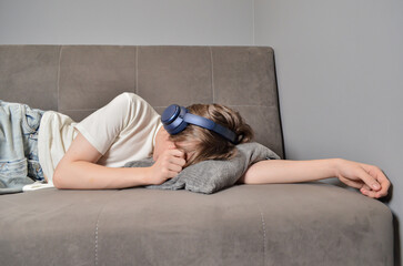 Obraz premium Young adult woman napping on sofa with headphones in living room