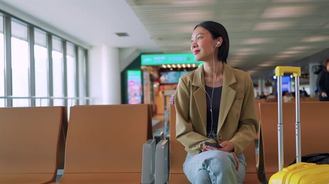 Asian woman starts her morning routine at the airport gate, listening to a podcast on her phone while waiting for departure. Concept of journey and solo travel. 