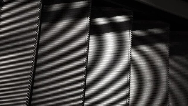 Close-up of escalator steps forming strong diagonal lines and repetitive metallic texture, creating an abstract pattern with light and shadow contrast