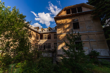 Fototapeta premium A striking view of Stalin’s abandoned wooden dacha in Tskaltubo, Georgia, showcasing decaying architecture overtaken by lush greenery, evoking history, mystery, and the passage of time. 