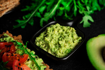 Obraz premium Avocado sandwich with avocado cream and rye crisp bread for snack. Fiber, fitness and diet food. Rye bread with guacamole, arugula and cherry tomatoes on dark background. High quality photo