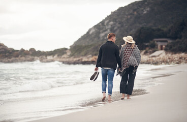 Love, couple and holding hands at beach on walk for care, connection and bonding on vacation. Man, woman and support by ocean on holiday, summer and space for healthy relationship with back view
