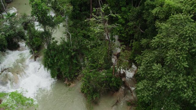 Airborn flying view of river running through tropical forest, with small cascades flowing though rock and stones along the stream