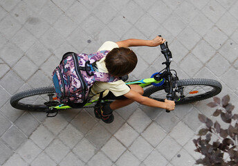 Bicicleta y niño ciclista escolar pedaleando con mochila de colegio en perspectiva aérea desde arriba