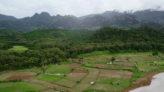 Forward flying high altitude airborne view of a narrow river and it coastline with large moutain formations in the bac kground, in overcast rainy weather.