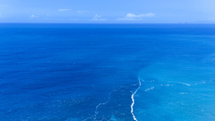 Obraz premium Aerial abstract view of deep blue and vibrant turquoise ocean waters with a gentle line of white sea foam.