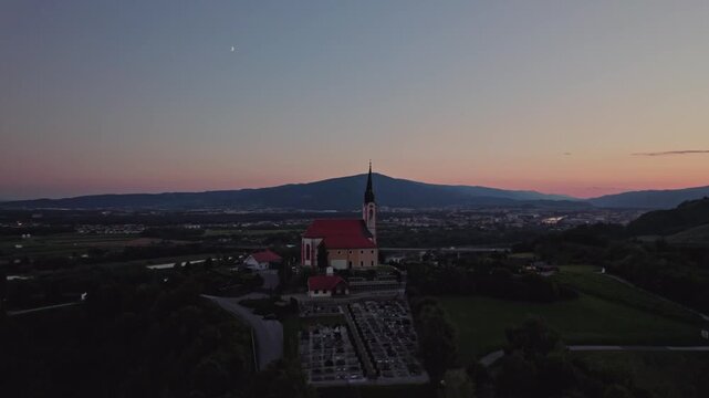 Gorca - Marijina cerkev v Malečniku , Slovenia - drone view on the church, river Drava and Maribor during sunset