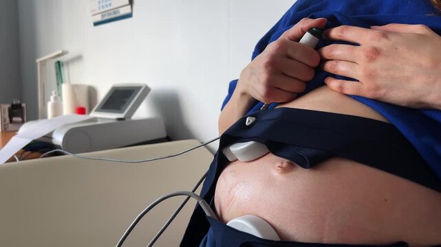 Expectant mother receiving a non-stress test in a medical clinic, with cardiotocography sensors strapped to her pregnant belly to check the baby's health and record heartbeats