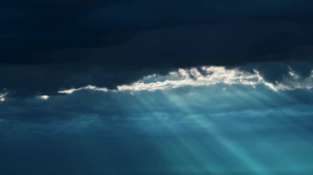 Sunbeams breaking through dark storm clouds in blue sky