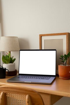 Vertical laptop mockup with blank white screen on wooden desk with chair, plants, and copy space for home office design.