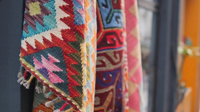 Colorful hand-woven textile art hangs vertically, showcasing intricate traditional patterns and vibrant hues under soft ambient lighting, creating a warm and inviting display