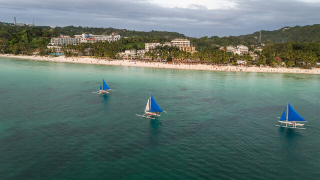 Aerial view of traditional Paraw sailboats sailing on the calm ocean at sunset in Boracay, Philippines. A beautiful tropical seascape during golden hour with vibrant orange sky