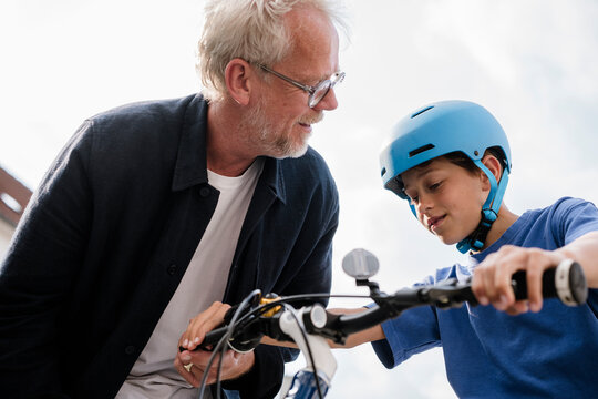 Father teaching son to ride bike outdoors with helmet and support