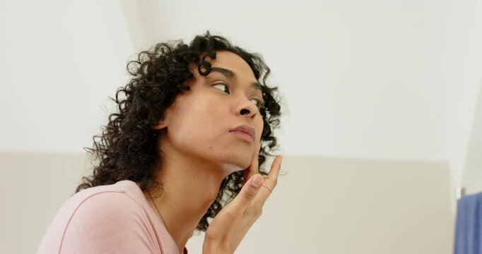 Non-binary adult noticing dry skin while dabbing and smoothing cream on cheek at dressing mirror