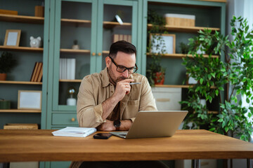 Obraz premium Man wearing eyeglasses working on laptop in home office