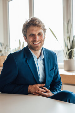 Smiling businessman in blue suit sitting in office by window