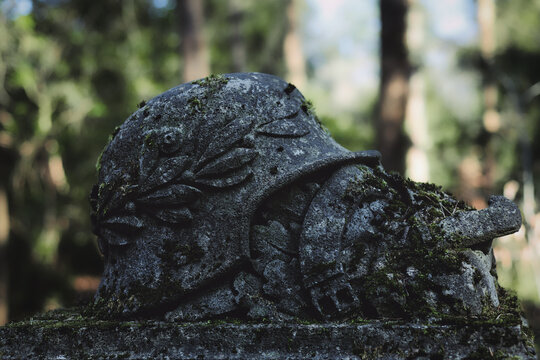 Antique Mossy Stone WWI German Helmet Memorial with Laurel Wreath and Sword - Somber War Commemoration in a Forest
