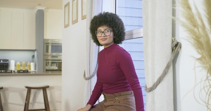 African American woman shifting, glancing out window smiling and laughing by pampas grass on ledge