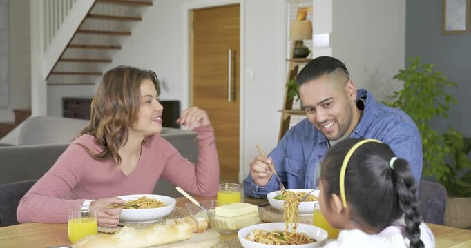 Family of three twirling spaghetti at dining table mother touching partner shoulder sparking banter