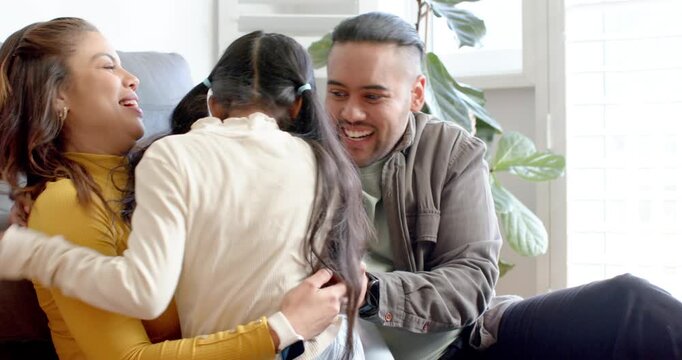 Diverse family sharing banter on sofa, raising arms excitedly, girl running into laps giggling