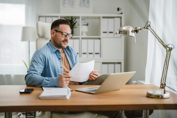 Obraz premium Man in glasses reviewing paperwork working from home office
